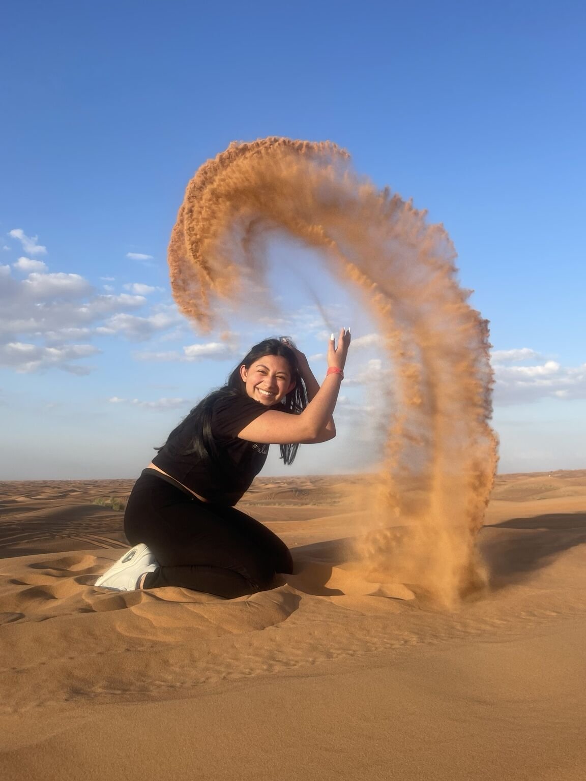 Guest creating a dramatic sand-toss photo in the Dubai desert